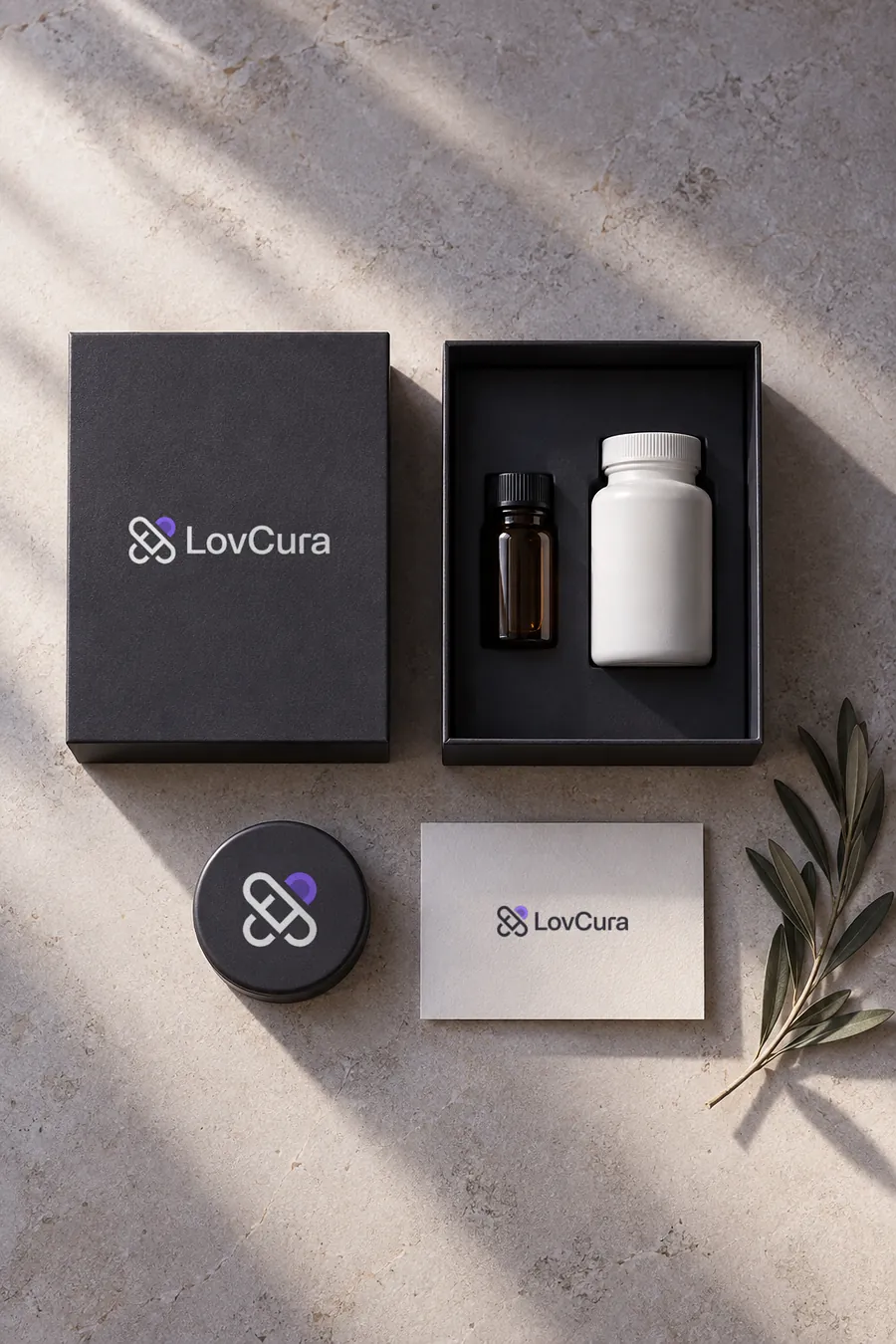 A charcoal LovCura box with an amber vial, a white bottle, a tin and a card on pale stone